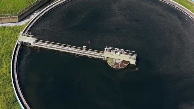 Circular Water Clarifier: An aerial view captures the circular tank of a water treatment plant, with a mechanical arm slowly rotating to skim the surface of the dark liquid.