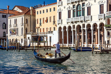 Traditional black gondola with a gondolier in a striped shirt rowing tourists along the Grand Canal in Venice, Italy © Nikolay N. Antonov