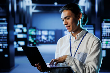 Qualified engineer in data center using laptop to prevent system overload during peak traffic...