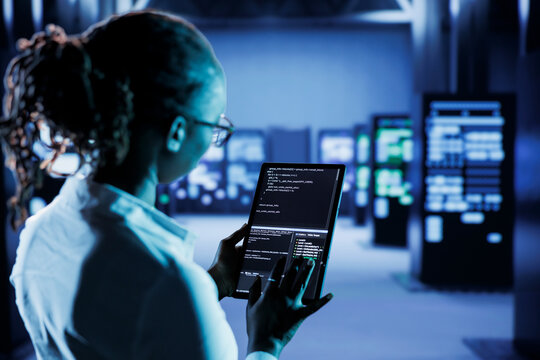 Computer scientist builds firewall protection systems in server room housing advanced infrastructure. High tech facility manager runs code on tablet to upgrade data center rigs