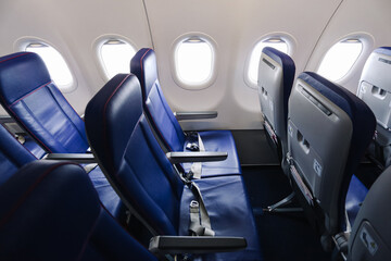 Obraz premium Empty airplane cabin seats aligned neatly. Blue leather chairs beside bright windows await passengers. Modern aircraft interior looks clean and calm. Travel transport scene suggests upcoming journey.