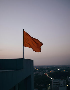 Orange flag waving on building rooftop at twilight over city