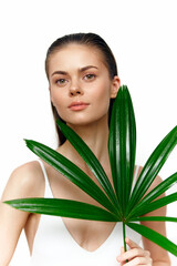 Naklejka premium Elegant young woman holding a tropical leaf, showcasing natural beauty and serenity against a white background for a fresh, vibrant concept.