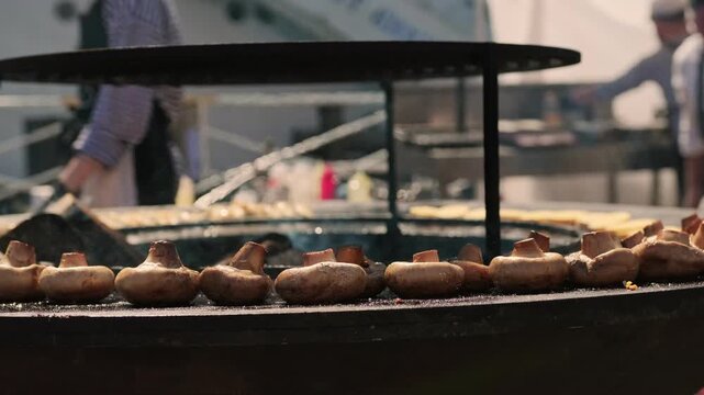 Mushroom cooking on round outdoor grill rack. Chef roasting vegetable on street food stall. Culinary preparation for summer picnic or festive barbecue party event. Healthy vegan meal.