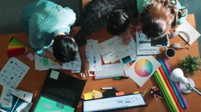 Top down aerial view of project manager looking at screen while designer writing idea. Smart business team explain idea of logo design while designer choose theme while looking at palette. Symposium.