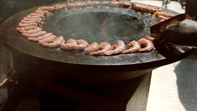 Shrimp cooking on outdoor charcoal circular grill. Seafood preparation on hot fire during street food festival. Culinary art and gourmet meal concept for dining event or party.