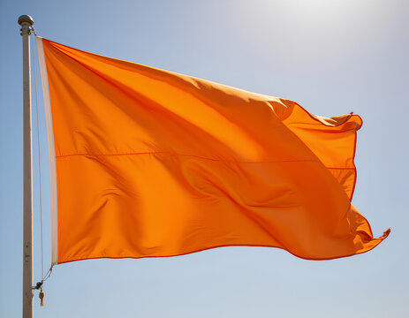 Bright orange flag waving on a pole against clear blue sky