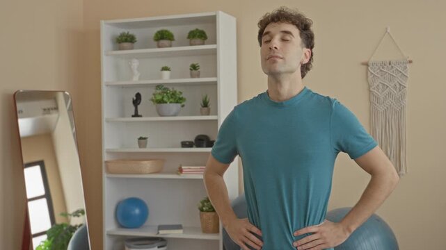Man standing with hands on hips and eyes closed beside exercise ball in studio; relaxation mindfulness.