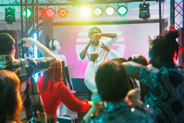 People on dancefloor moving to rhythm at electronic music concert in nightclub. Crowd partying,...