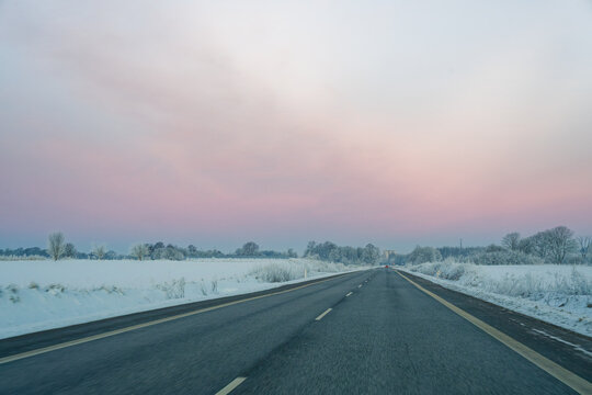 Empty highway road in Kollund DK stretching through snowy winter landscape under pastel sky