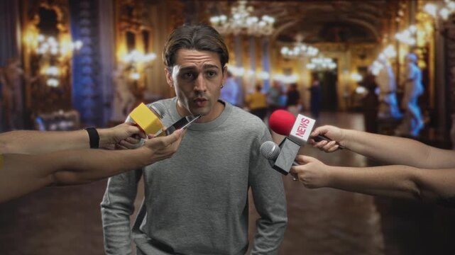 Man answering questions while multiple reporters hold microphones to his mouth and chin in an ornate building lobby; nervousness.