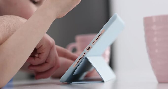 Father and his son using tablet at white table indoors, closeup