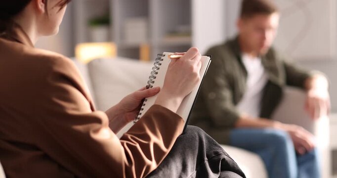 Professional psychologist making notes during therapy session with patient indoors, selective focus