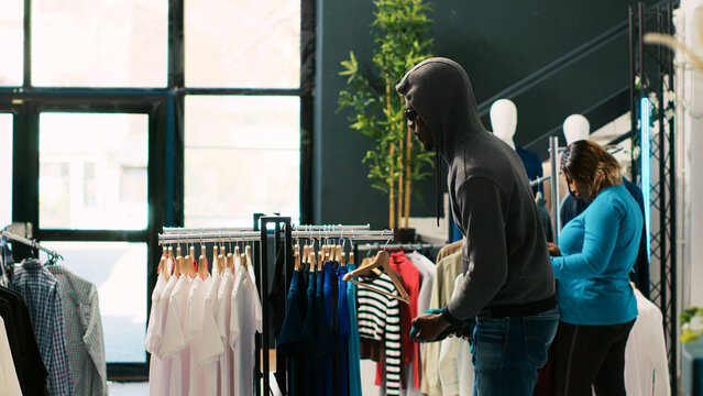 African american robber stealing fashionable outfit, trying to run from shopping mall. Asian bodyguard catch thief at boutique door, asking him to return stylish clothes or will call the police