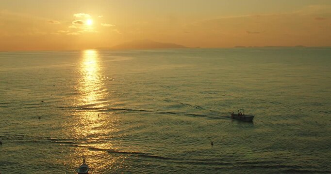 Fishing boat sailing on calm water during golden sunset at Capri Island coast Italy