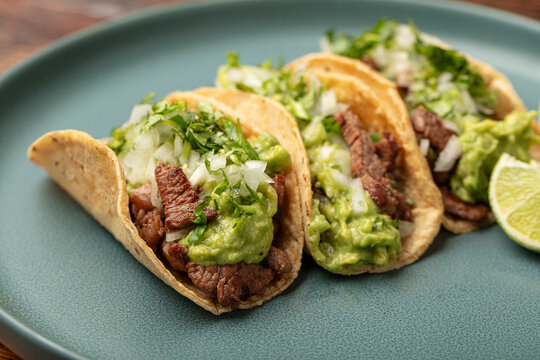 Three Mexican carne asada steak street tacos on a plate with onions, cilantro, carne asada and guacamole on corn tortillas