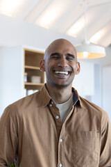 Obraz premium Man smiling eyes-closed in kitchen under pendant lamp with beams and shelving, wearing brown shirt