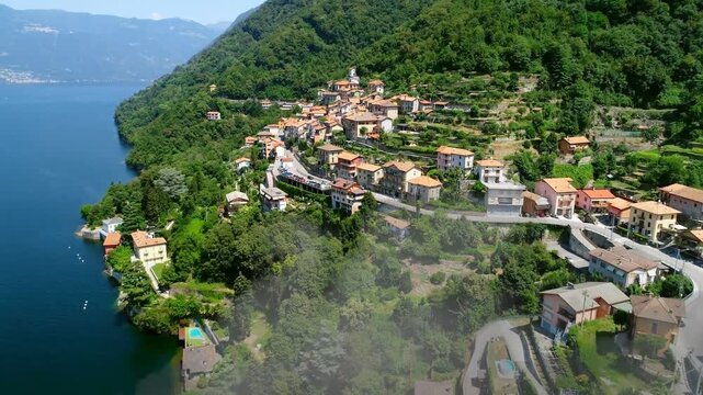 Drone approaching hillside village, mist drifting from lake, showing terraced roofs for tourism