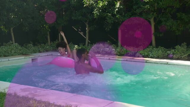 Woman floating on pink donut pool man jumping causing splash tossing ball playing leisure overlays