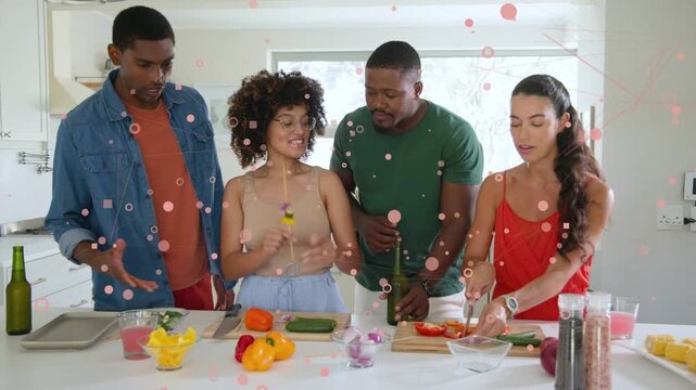 Right woman starting slicing tomatoes, group making food skewers on island, pink overlays obscuring