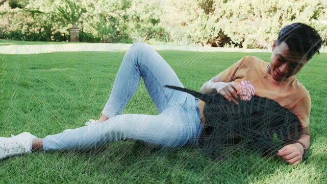 Man reclining on grassy lawn waving pink rope toy, enticing dog and promoting pet care bonding