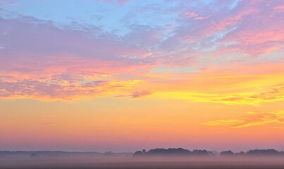 Fototapeta premium Misty dawn landscape with colorful sky transitioning from pink to yellow