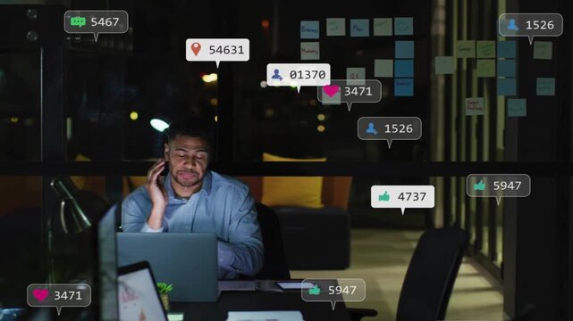Man working late in glass office, receiving social media likes messages alert badges over laptop