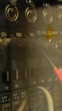 Vertical close-up of backstage audio patch panel with connected cables, labeled ports, and warm stage lighting, capturing technical theater signal routing and live production infrastructure.