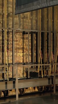 Vertical view of a theater curtain rising beside fly-system ropes and metal frames, revealing backstage rigging and warm brick textures in a technical stage space.