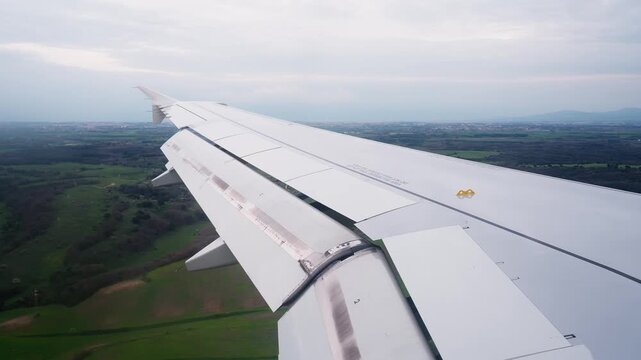 Passenger-window view of an airplane wing during descent over green countryside, capturing commercial air travel, approach landing, and in-flight journey atmosphere.