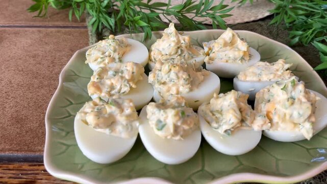 Close-up of homemade deviled eggs on a leaf-shaped platter, styled as a rustic party appetizer with creamy herb filling and fresh decorative greenery.