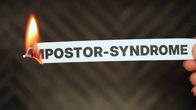 Burning &ldquo;impostor-syndrome&rdquo; label held by hand, symbolizing self-confidence, earned success, self-trust, and freedom from self-doubt, insecurity, and feeling undeserving.