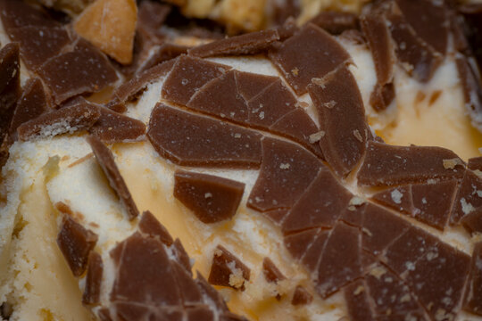 Detail close up of fragmented milk chocolate pieces embedded in soft vanilla ice cream on a dessert, showing texture and cocoa details