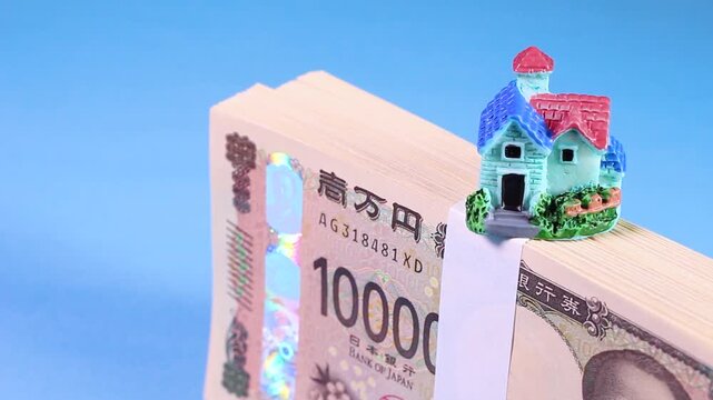 水色背景で回転する新紙幣の札束とミニチュアハウスの模型