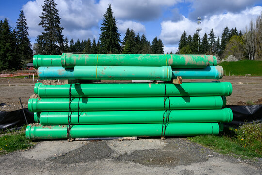Construction site at earthworks stage, stack of large diameter green PVC pipe delivered to job and ready for underground water utility system installation
