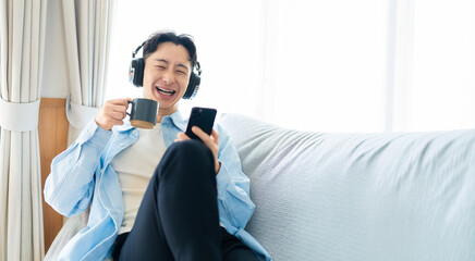 スマートフォンで音楽や動画を楽しみながらくつろぐ男性, Man Relaxing on Sofa Enjoying Music or Videos on Smartphone © Trickster*