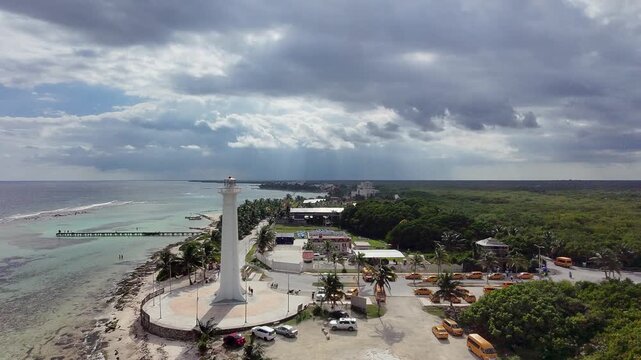 Aerial drone view of Faro de Mahahual lighthouse on the Caribbean coast in Mahahual, Quintana Roo, Mexico, with turquoise sea, tropical shoreline, and dramatic clouds.