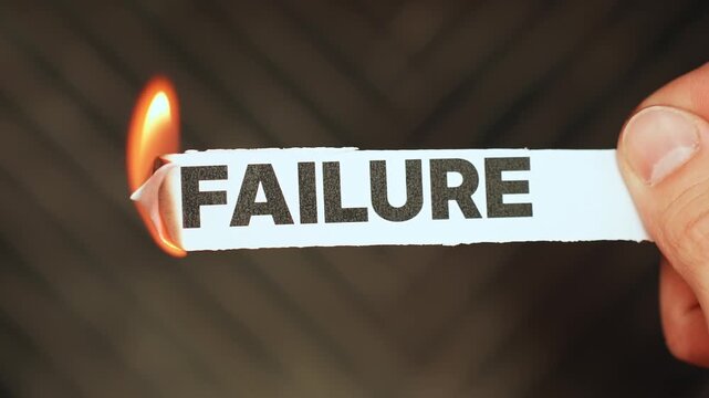 Burning &ldquo;failure&rdquo; label held by hand, symbolizing overcoming setbacks, resilience, breakthrough mindset, and turning defeat into progress and success.