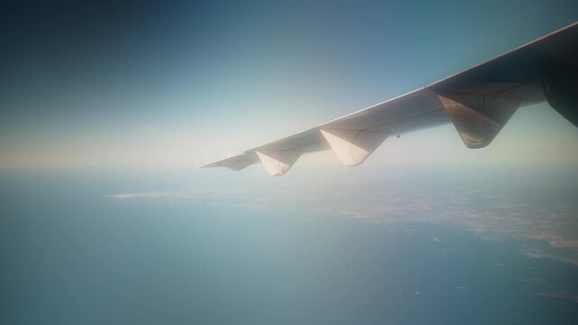 Dreamlike airplane-wing view above open sea and coastline, capturing the feeling of flying, freedom, and faraway travel in soft atmospheric light.