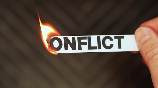 Burning &ldquo;conflict&rdquo; label held by hand, symbolizing peace, reconciliation, resolution, and leaving arguments, tension, and division behind.