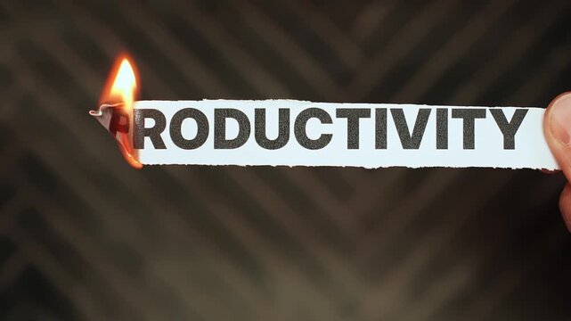 Burning &ldquo;productivity&rdquo; label held by hand, symbolizing procrastination, distraction, burnout, and the collapse of efficiency, output, and work momentum.