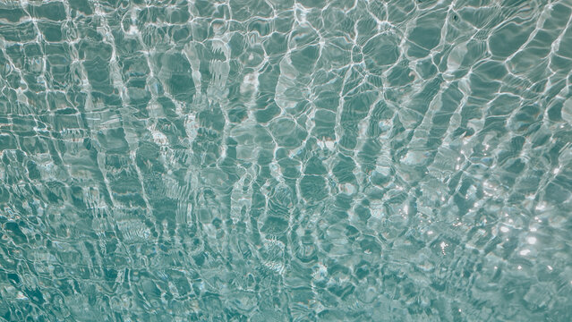 Sunlight reflecting through clear swimming pool water creating abstract caustic patterns on the blue floor. Abstract wallpaper, backdrop, background.