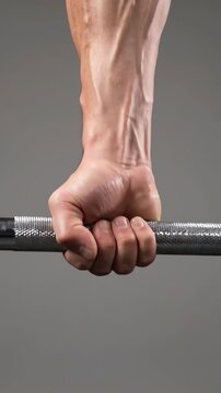 Close-up of a muscular, veiny male hand gripping a heavy barbell against a gray background.