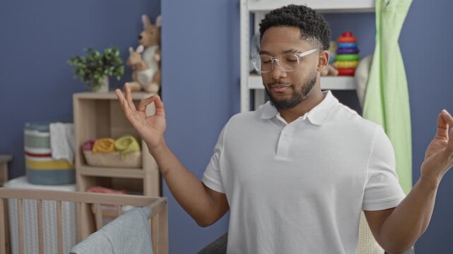 Man in white polo with hands in meditative ok gesture beside wooden baby crib and toy shelf in nursery; calm bonding.