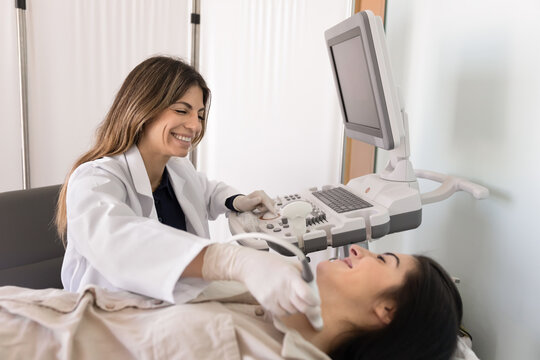 Smiling female endocrinologist checking woman patient thyroids gland nodules using ultrasonography equipment, scanning, review endocrine system during visit at clinic. Preventive medicine, insurance