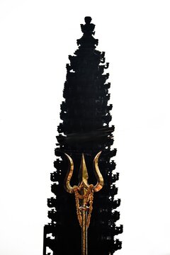 Golden Trishula Trident in Front of Hindu Temple Silhouette Against White Sky