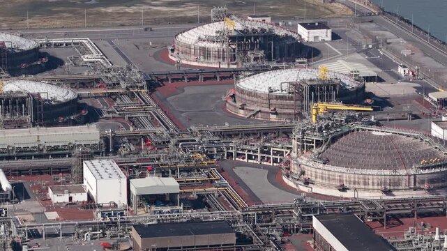 High angle view capturing an expansive liquefied natural gas terminal, showing massive storage tanks, intricate pipelines, and industrial infrastructure at a coastal processing facility