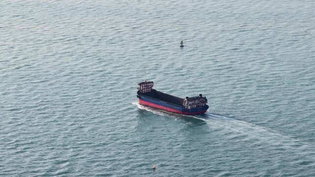 Aerial view of a large, empty bulk carrier ship navigating across the open ocean, leaving a white wake behind it on the blue green water as it transports goods for international trade