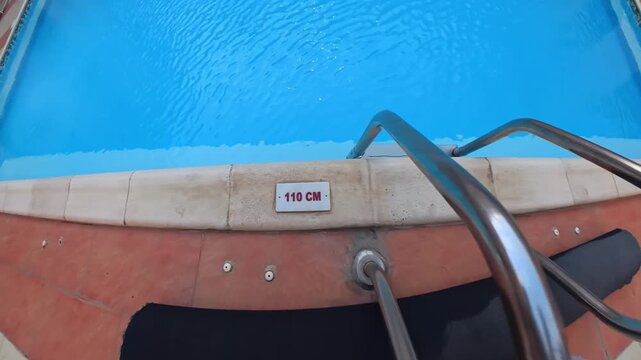 Top-down poolside view of a little girl holding the ladder beside 110 cm deep water, capturing family resort safety, supervised play, and child-focused vacation moments.