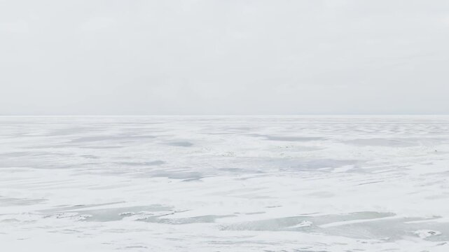 Two bundled figures, adult and child, walk onto a foggy winter beach facing a frozen ocean. Minimal scene with strong copy space, safety risk and climate warming mood.